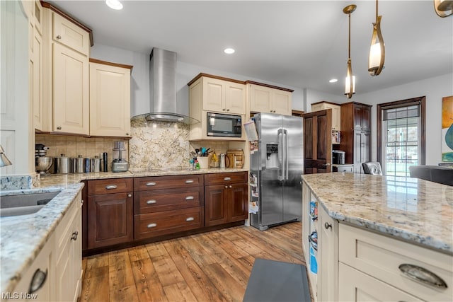 kitchen with appliances with stainless steel finishes, light hardwood / wood-style flooring, wall chimney range hood, hanging light fixtures, and decorative backsplash