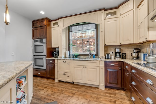 kitchen featuring light hardwood / wood-style flooring, backsplash, light stone counters, stainless steel double oven, and decorative light fixtures