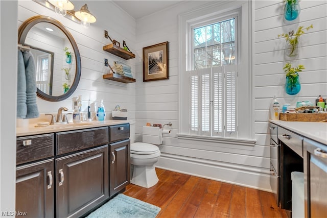 bathroom with wood walls, vanity, toilet, and hardwood / wood-style floors