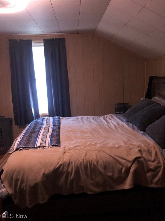 bedroom featuring vaulted ceiling and wooden walls