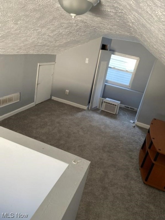 bonus room featuring vaulted ceiling, a textured ceiling, a wall unit AC, and carpet floors