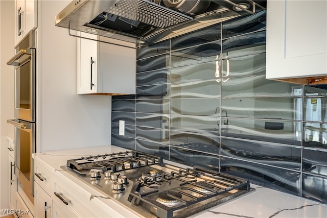 kitchen with white cabinets, appliances with stainless steel finishes, light stone counters, and exhaust hood