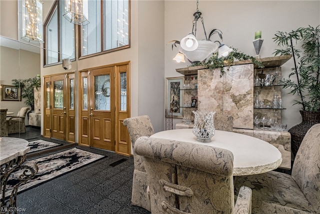 dining room featuring dark tile flooring, a chandelier, a healthy amount of sunlight, and a towering ceiling