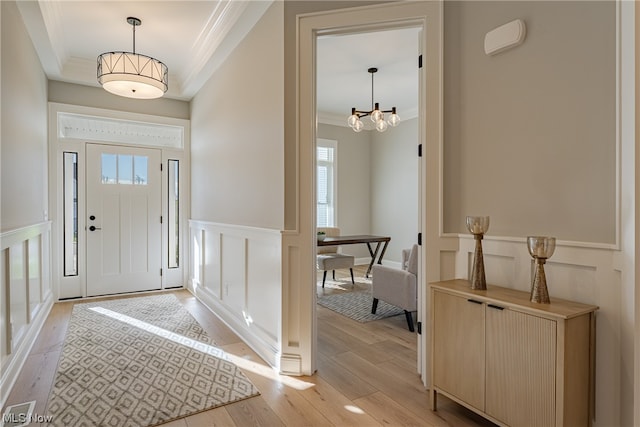 entryway featuring light hardwood / wood-style flooring, a notable chandelier, a raised ceiling, and plenty of natural light