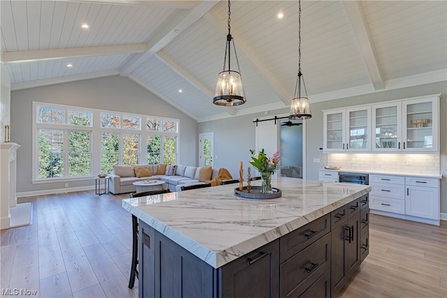 kitchen with backsplash, a barn door, light hardwood / wood-style floors, white cabinets, and light stone counters