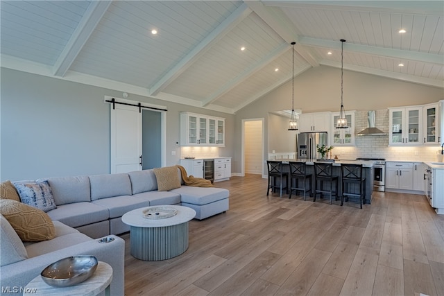 living room featuring beamed ceiling, a barn door, high vaulted ceiling, light hardwood / wood-style floors, and wooden ceiling