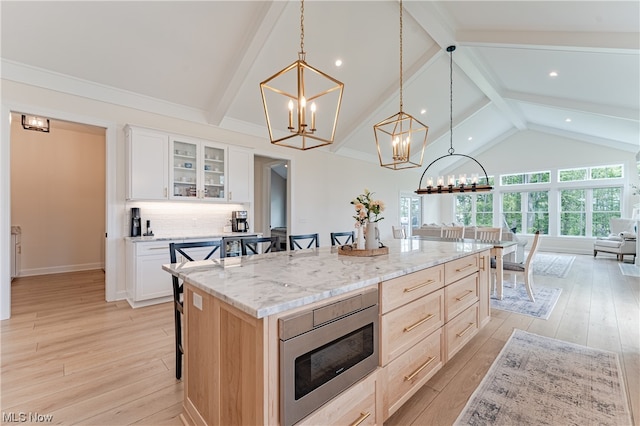 kitchen featuring light hardwood / wood-style floors, white cabinetry, a kitchen island, stainless steel microwave, and beam ceiling