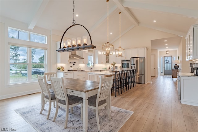 dining space with beamed ceiling, a notable chandelier, sink, high vaulted ceiling, and light hardwood / wood-style flooring