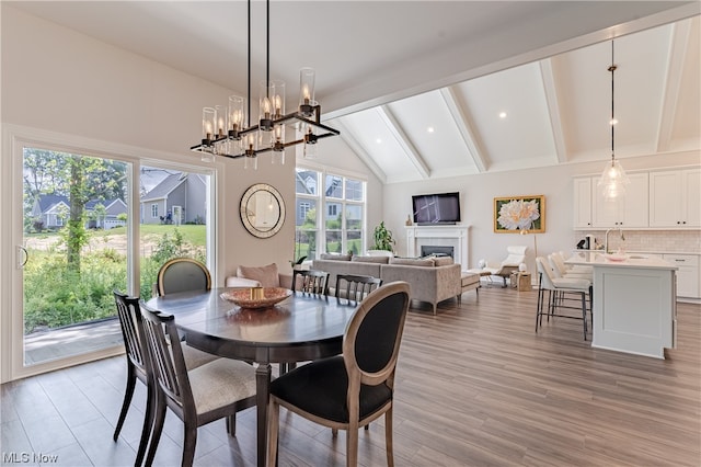 dining room featuring beam ceiling, a chandelier, sink, and light hardwood / wood-style flooring