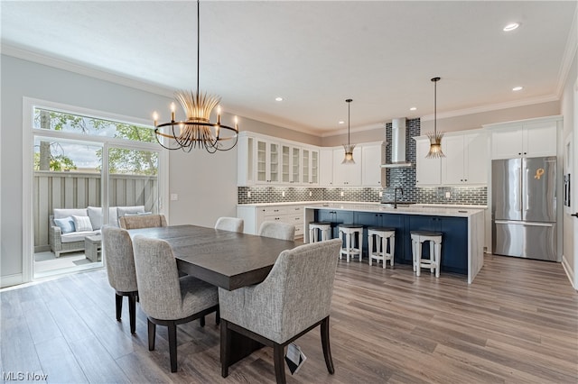 dining area with light wood-type flooring, crown molding, sink, and a chandelier