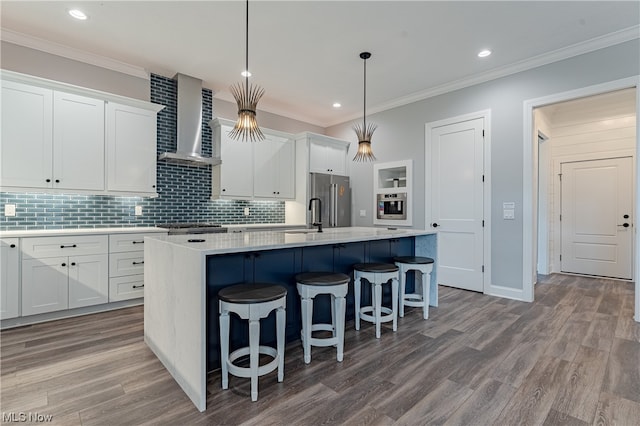 kitchen featuring hardwood / wood-style flooring, a kitchen island with sink, wall chimney exhaust hood, hanging light fixtures, and high end refrigerator