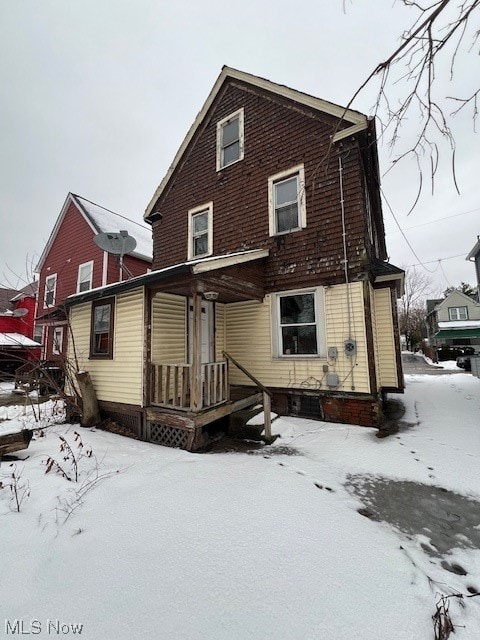 snow covered rear of property featuring covered porch