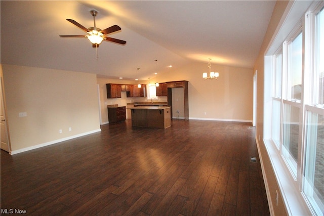 unfurnished living room featuring a wealth of natural light, dark wood-type flooring, vaulted ceiling, and ceiling fan with notable chandelier