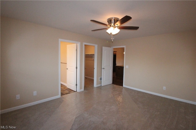 unfurnished bedroom featuring a closet, a walk in closet, dark carpet, and ceiling fan