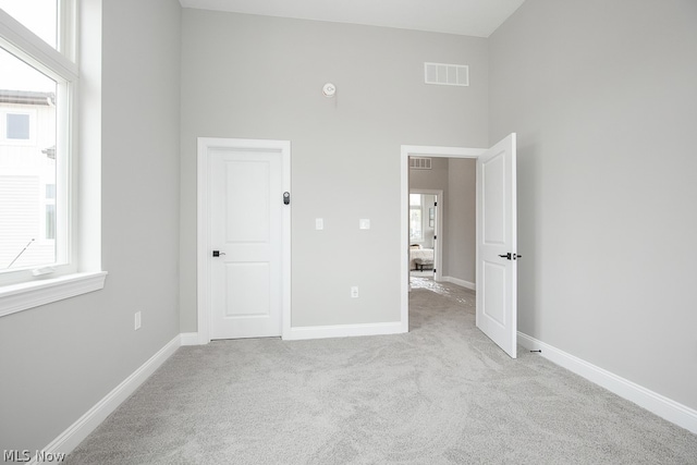 unfurnished bedroom with light carpet, multiple windows, and a high ceiling