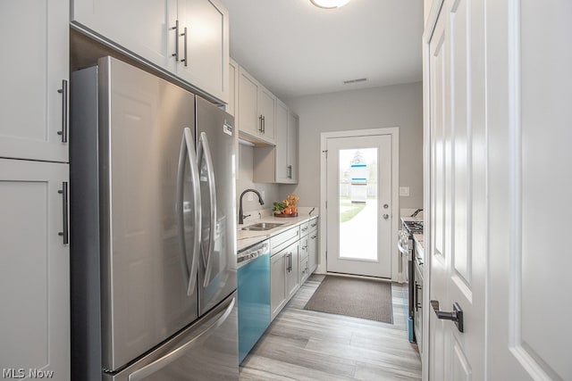 kitchen with appliances with stainless steel finishes, light hardwood / wood-style flooring, white cabinets, and sink