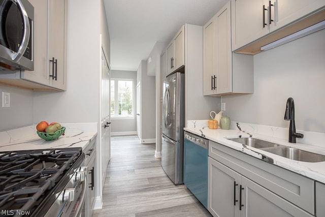 kitchen featuring light stone counters, appliances with stainless steel finishes, sink, gray cabinetry, and light wood-type flooring