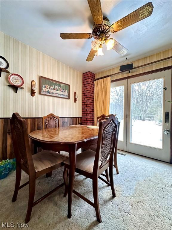 dining space featuring ceiling fan, light colored carpet, and wood walls