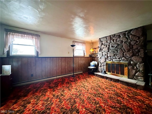 unfurnished room featuring a stone fireplace, wood walls, carpet, and a baseboard heating unit