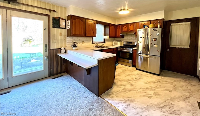 kitchen with kitchen peninsula, appliances with stainless steel finishes, tasteful backsplash, a breakfast bar, and sink