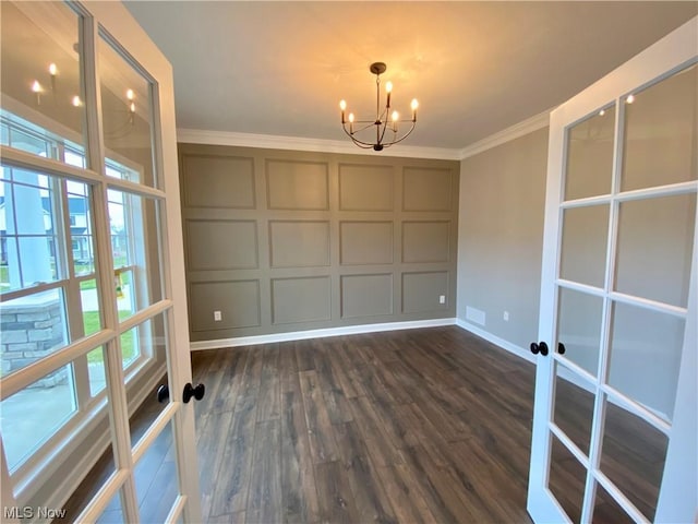 unfurnished dining area featuring dark wood-style flooring, an inviting chandelier, crown molding, french doors, and a decorative wall