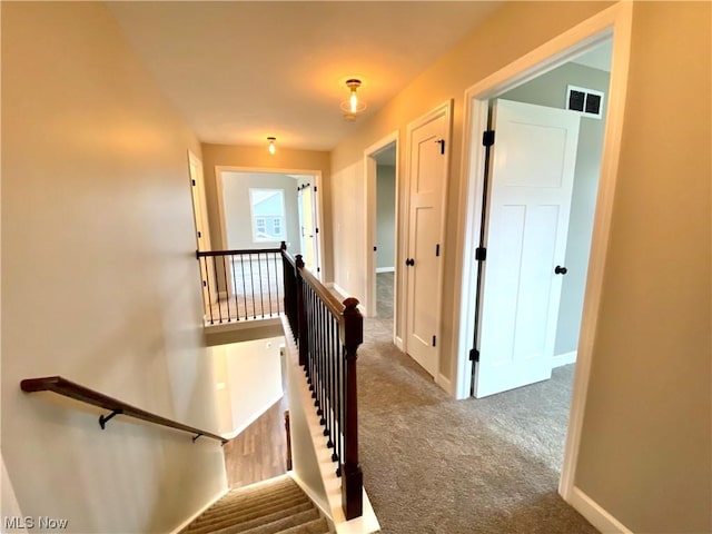 corridor featuring visible vents, carpet floors, an upstairs landing, and baseboards