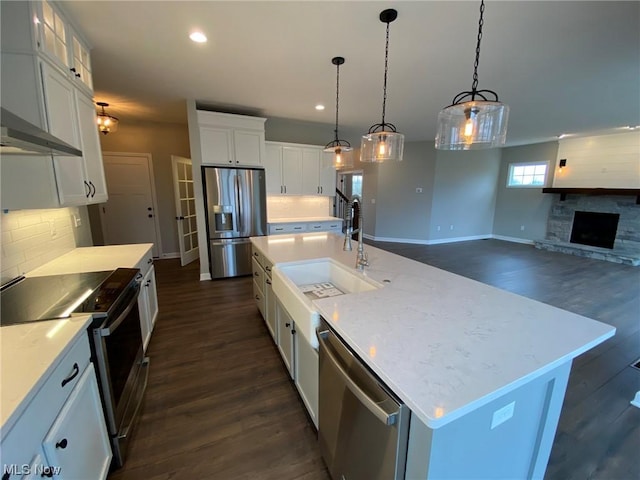 kitchen featuring white cabinets, an island with sink, open floor plan, hanging light fixtures, and stainless steel appliances