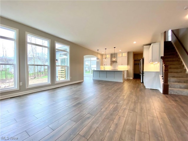 unfurnished living room featuring baseboards, arched walkways, dark wood-type flooring, stairs, and recessed lighting