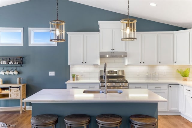 kitchen featuring stainless steel gas range, a kitchen island with sink, lofted ceiling, white cabinetry, and a breakfast bar area