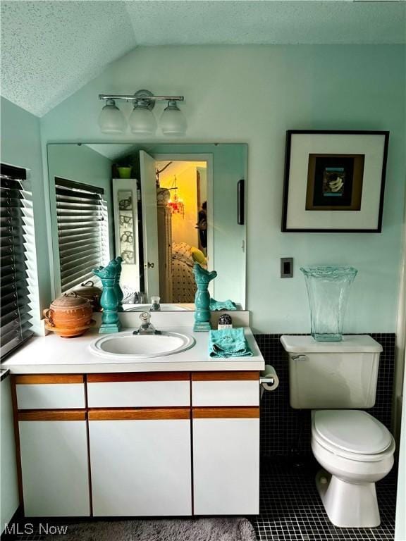 bathroom featuring a textured ceiling, lofted ceiling, tile patterned flooring, toilet, and vanity