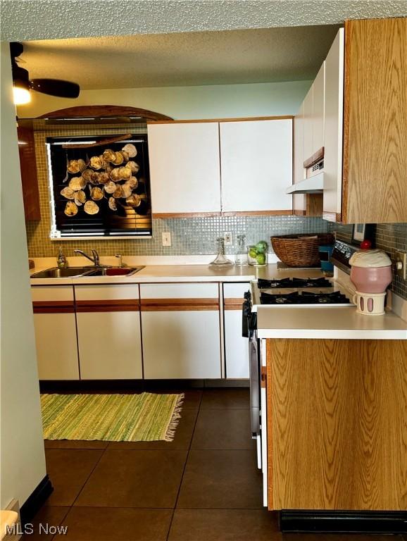 kitchen with under cabinet range hood, a sink, light countertops, backsplash, and range with gas cooktop