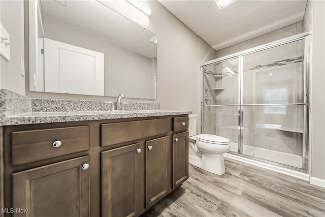 bathroom featuring vanity, hardwood / wood-style floors, a shower with shower door, and toilet