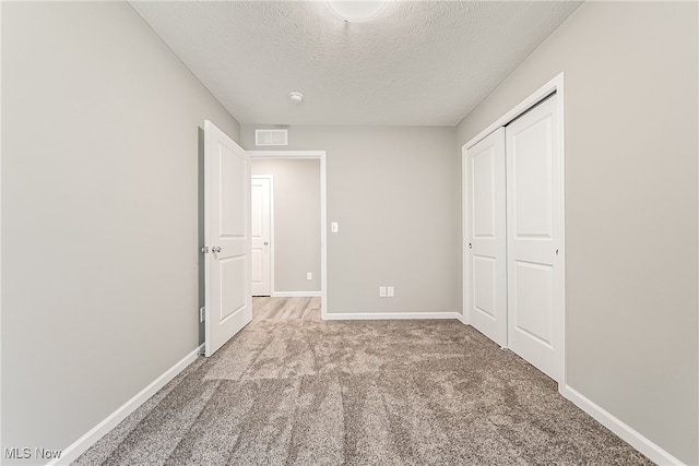 unfurnished bedroom featuring light carpet, a textured ceiling, and a closet