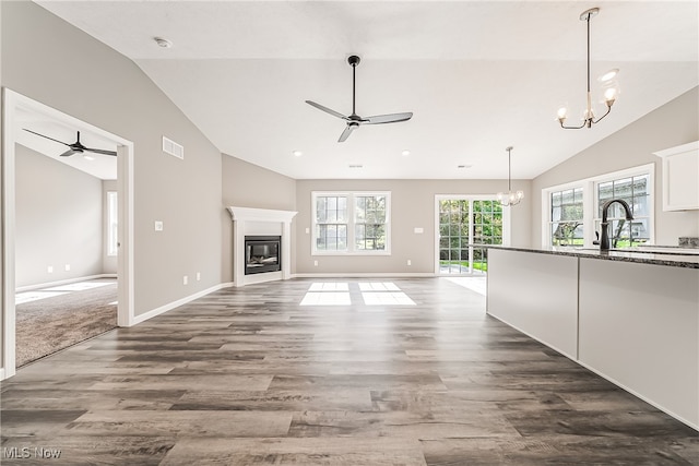 unfurnished living room with lofted ceiling, dark hardwood / wood-style floors, and ceiling fan with notable chandelier