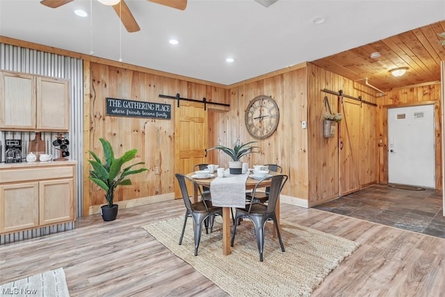 dining room featuring a barn door, wood walls, tile flooring, and ceiling fan