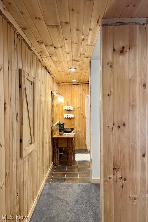 hallway with wooden walls, dark tile flooring, and wooden ceiling