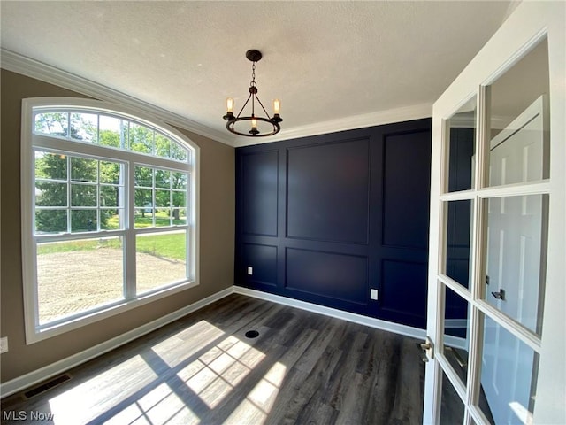 unfurnished dining area featuring crown molding, dark wood finished floors, visible vents, a decorative wall, and a chandelier