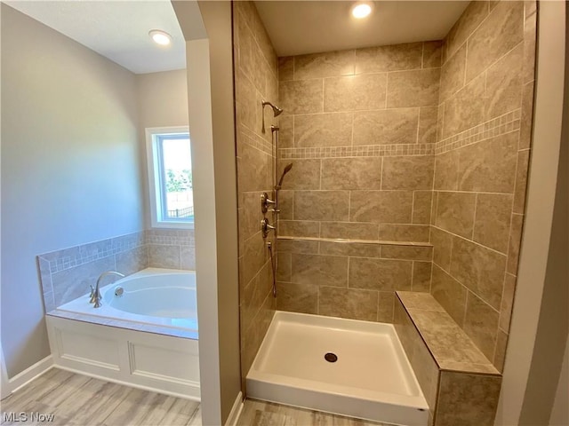 bathroom with wood finished floors, a shower stall, a bath, and baseboards