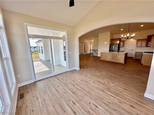 unfurnished living room featuring hardwood / wood-style flooring, lofted ceiling, and an inviting chandelier