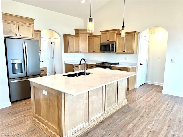 kitchen with arched walkways, a sink, appliances with stainless steel finishes, an island with sink, and pendant lighting