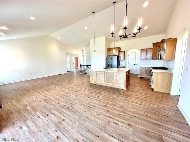 kitchen featuring a kitchen island with sink, stainless steel appliances, open floor plan, light countertops, and decorative light fixtures