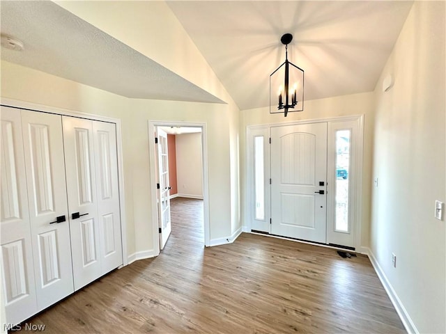 entrance foyer featuring lofted ceiling, baseboards, a chandelier, and wood finished floors