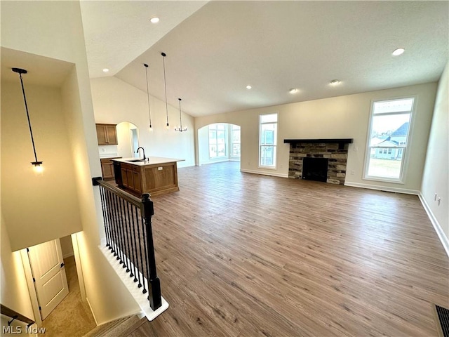 living room with baseboards, arched walkways, wood finished floors, a stone fireplace, and recessed lighting