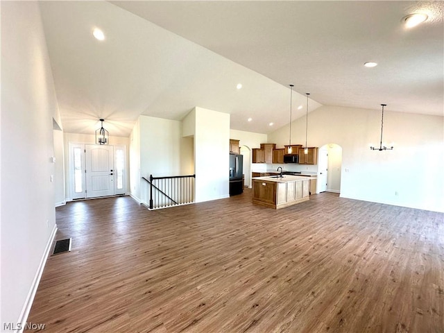 unfurnished living room with an inviting chandelier, lofted ceiling, dark hardwood / wood-style flooring, and sink