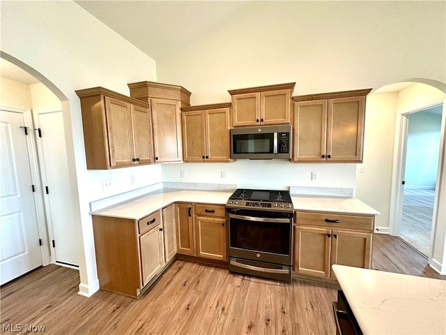 kitchen with high vaulted ceiling, appliances with stainless steel finishes, and light hardwood / wood-style floors