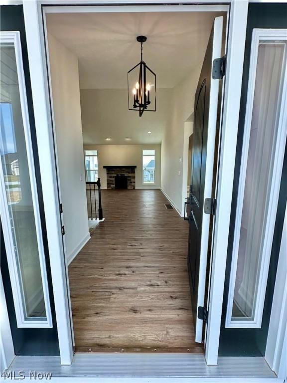 interior space with a chandelier, a fireplace, wood finished floors, visible vents, and baseboards