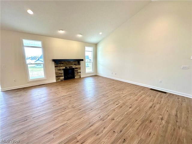 unfurnished living room featuring lofted ceiling, a fireplace, light wood-style flooring, and a healthy amount of sunlight