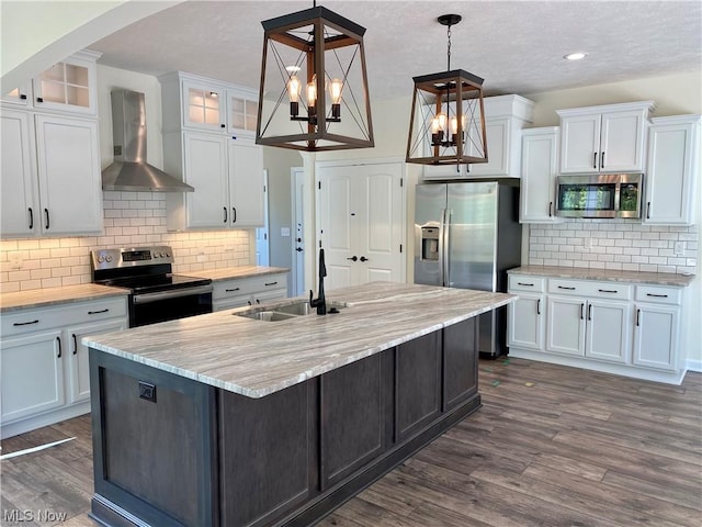 kitchen featuring stainless steel appliances, white cabinetry, wall chimney exhaust hood, glass insert cabinets, and pendant lighting