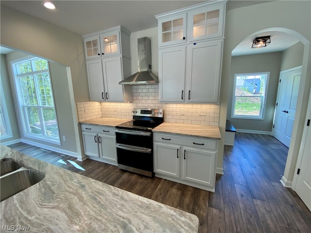 kitchen with light stone counters, dark wood-type flooring, electric stove, wall chimney range hood, and white cabinets