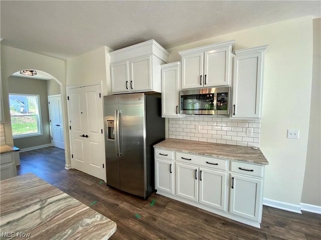 kitchen featuring dark wood-style floors, arched walkways, tasteful backsplash, appliances with stainless steel finishes, and white cabinetry